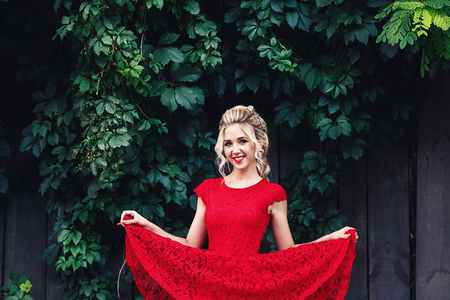 attractive young blonde girl in red dress posing near a wild vineyardの写真素材