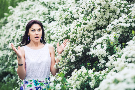 very surprised girl smiles broadly in nature among flowering spirea bushes.