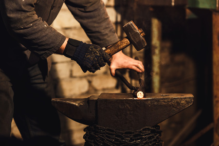 The blacksmith manually forging the red-hot metal on the anvil in smithy