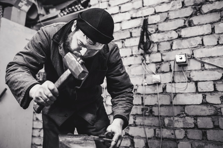 The blacksmith manually forging the red-hot metal on the anvil