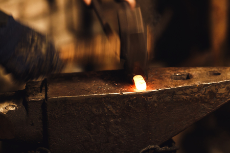 The blacksmith manually forging the red-hot metal on the anvil in smithyの写真素材