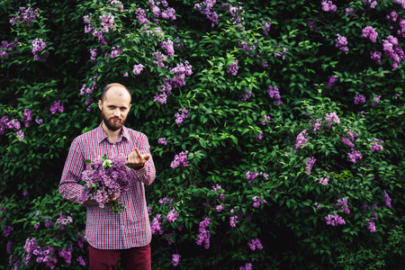 man calls to himself. young bearded man with a bouquet of flowers near lilac blossomsの写真素材