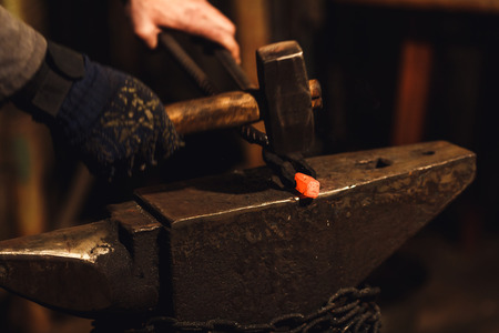 The blacksmith manually forging the red-hot metal on the anvil in smithyの写真素材