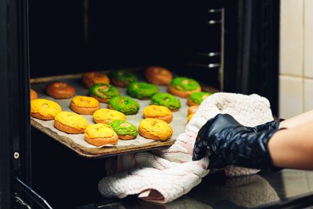 confectioner takes out a baking sheet with round green and yellow eclairs from the oven. Crispy...