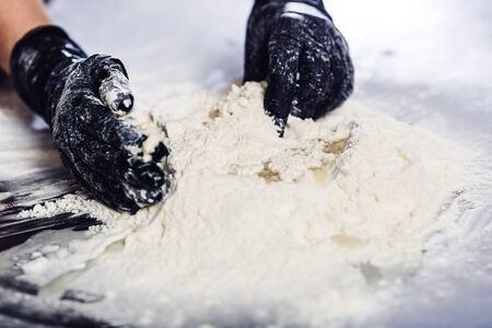 bakers hands in black gloves knead the dough.の写真素材