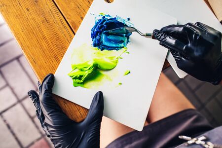 pastry chef in black rubber gloves stirs colored cream with spatula to decorate cake. food coloring...