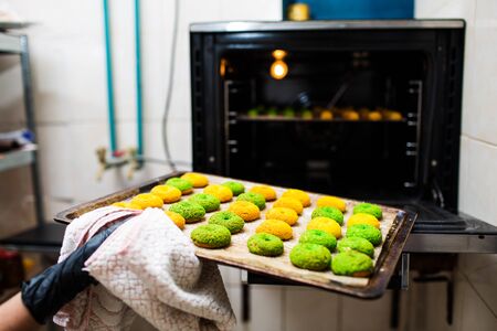 confectioner takes out a baking sheet with round green and yellow eclairs from the oven. Crispy Craquelure Profiterolesの写真素材