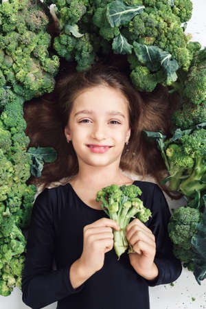 little girl lies among broccoli and holds with smiling. vegan healthy organic food conceptの写真素材
