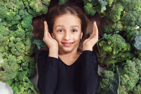 cheerful child girl lies among broccoli and laughs. nutrition and healthy eating habits for kids concept. hair and skin healthの写真素材