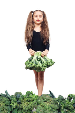 Cute girl in leotard stands among broccoli and holds it in her hands. Isolated on white backgroundの写真素材