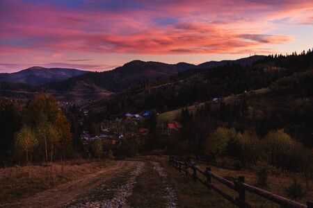 Beautiful mountain landscape with sunset illuminated sky. outgoing road with view of village between...
