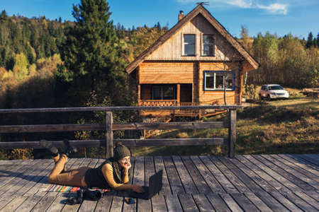 Beautiful girl with glasses lies on plaid in fall on wooden terrace and works on laptop. concept of...