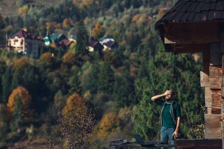 bearded freelancer laughs near log house against backdrop of mountain villageの写真素材