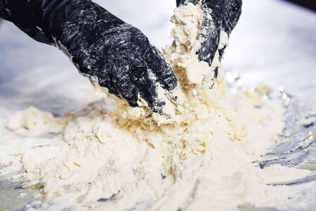 baker's hands in black gloves knead the doughの写真素材