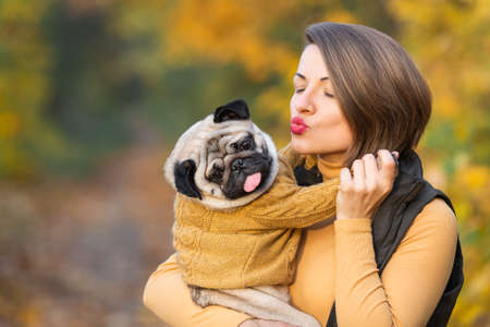 girl kisses a pug in the autumn in the park.の写真素材