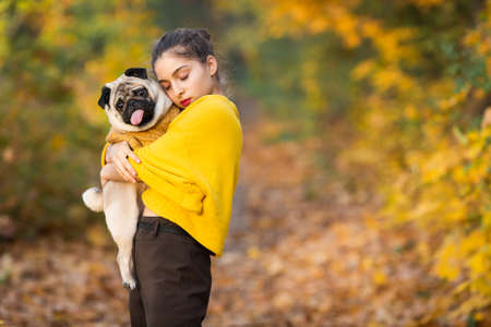 Teen girl with her dog pug in the autumn in the park.の写真素材