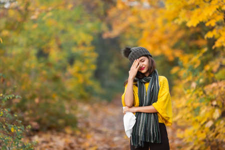 girl sneezes into a headscarf in autumn in the park. allergy or viral infection concept.