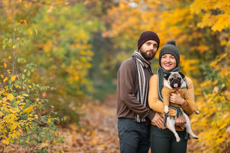 happy Family with a dog pug in the autumn forest throws leaves.の写真素材