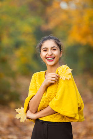 Cheerful woman portrait with autumn maple leaves in the park.