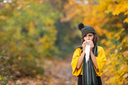 girl sneezes into a headscarf in autumn in the park. allergy or viral infection concept.