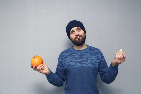 A bearded guy holds an orange and a suppository for hemorrhoids in his hands. Hemorrhoids conceptの写真素材