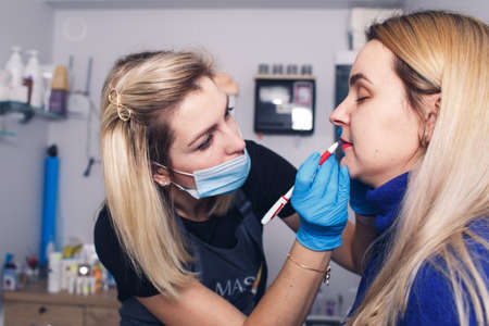 The beautician prepares the lips for permanent makeup, the model looks in the mirror.の写真素材