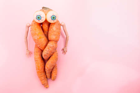 funny ugly twisted carrot on a pink background. Carrots with hands and eyes for your advertisementの写真素材