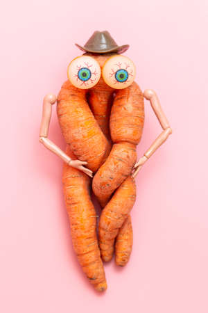 funny ugly twisted carrot on a pink background. Carrots with hands, eyes and a hat. Vegetable toyの写真素材