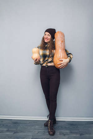 cheerful girl holding large and small pumpkin on gray backgroundの写真素材