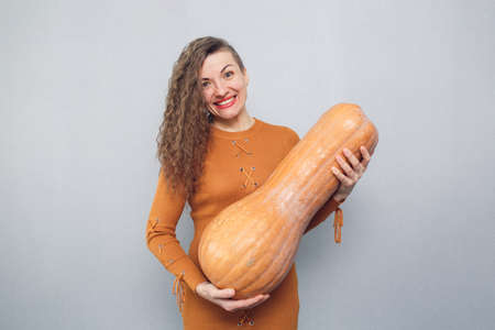 cheerful girl holding a large long pumpkin on a gray backgroundの写真素材
