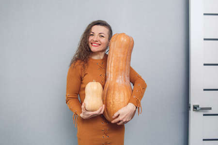 cheerful girl holding large and small pumpkin on gray backgroundの写真素材