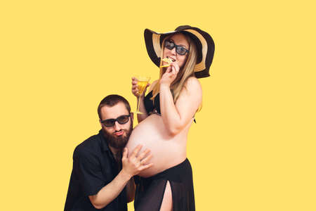 bearded man hugging belly of pregnant wife on isolated yellow background. The concept of the prenatal period. A young family is expecting a baby.の写真素材