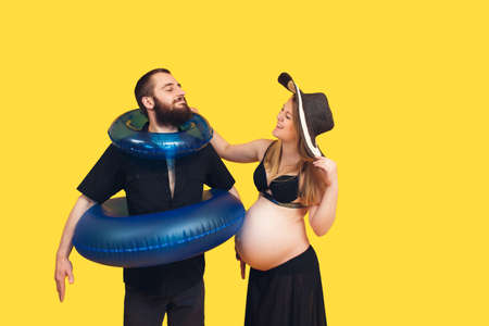 a pregnant girl puts swim rings on her husband. concept of summer vacation at sea