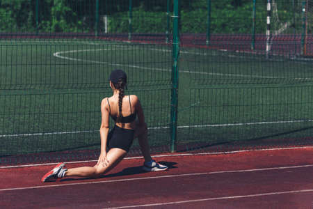 young woman doing deep lunge stretching on sports ground outdoors in summer.の写真素材