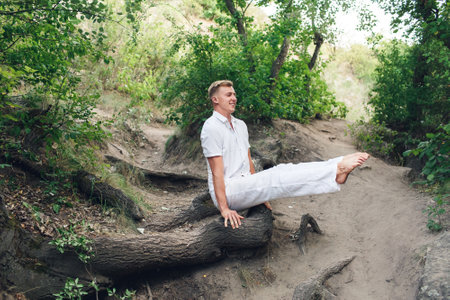 A young man practices yoga and performs a corner stand on the roots of an old treeの写真素材