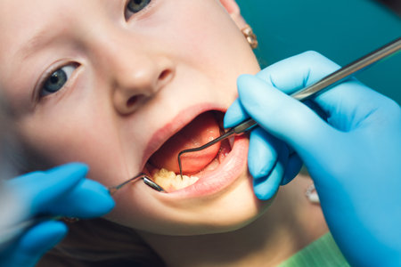a cute little girl sits in a dental chair with her mouth open while being examined by a doctor.の写真素材