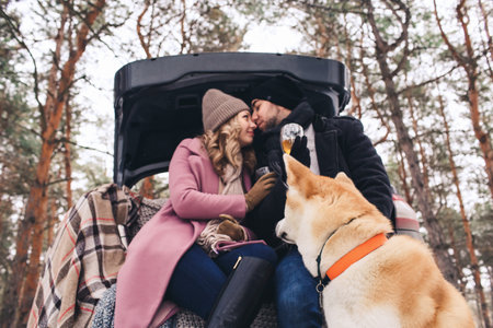 A beautiful couple kisses while sitting in the trunk of a car in the winter season, the dog sits nearby.の写真素材
