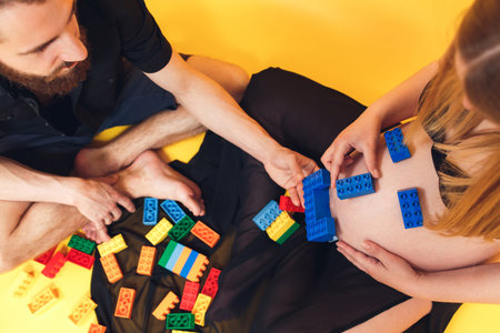 Husband creates emoji from childrens construction blocks on the belly of his pregnant wifeの写真素材