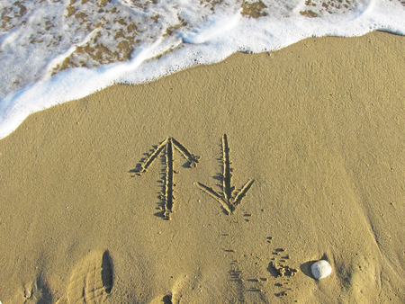 Arrows up and down drawn in the sandの写真素材