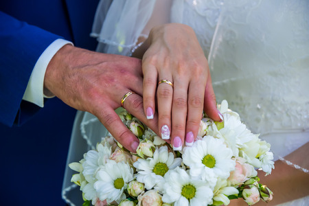 Hands of people on a bouquet of flowers, wedding ringsの写真素材
