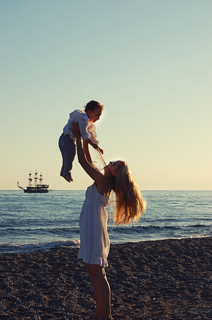 mother with child on the beach in Side, Turkey, against the background of the sea old shipの写真素材