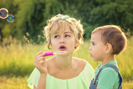 mother with her son and soap bubbles in the park, the family is resting on nature having fun and playingの写真素材