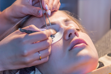 girl glues eyelashes at home with warm lightの写真素材