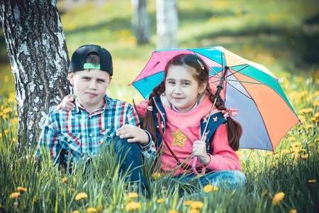 children walk in the park with an umbrella, a boy and a girl amicably walking in the summer with a colored umbrellaの写真素材