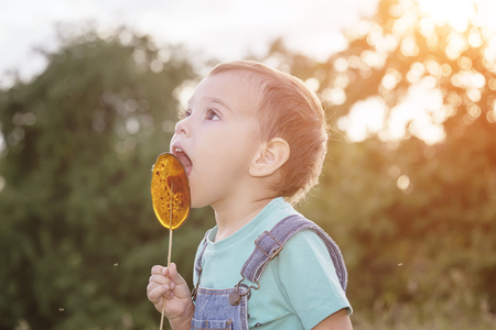 baby boy with a lollipop on his wand in his hands walking along the grass in a park in the natureの写真素材