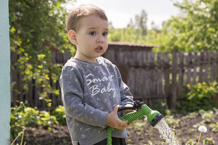 a child in the garden watering flowers, a little boy with a water hose watering the gardenの写真素材