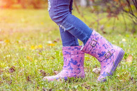 children's feet in rubber boots on yellowed dry grass in autumn