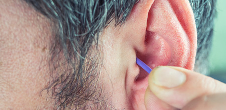 a man with a beard cleans his ears with a cotton swab to clean