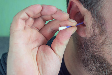 a man with a beard cleans his ears with a cotton swab to clean