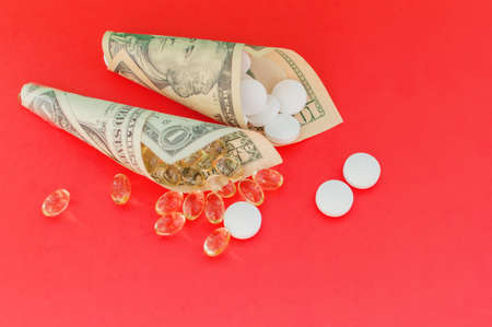 Medicines, vitamins and antioxidant supplements wrapped in money on a red background. The concept of expensive treatment. Close up.の写真素材